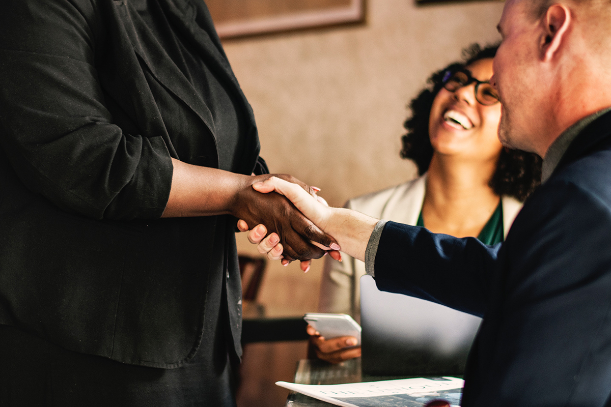 Two people shaking hands while a woman smiles in the background