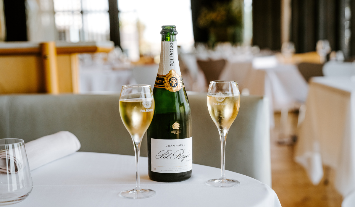 A close-up shot of a bottle of Champagne and two filled glasses atop a white tablecloth-covered table