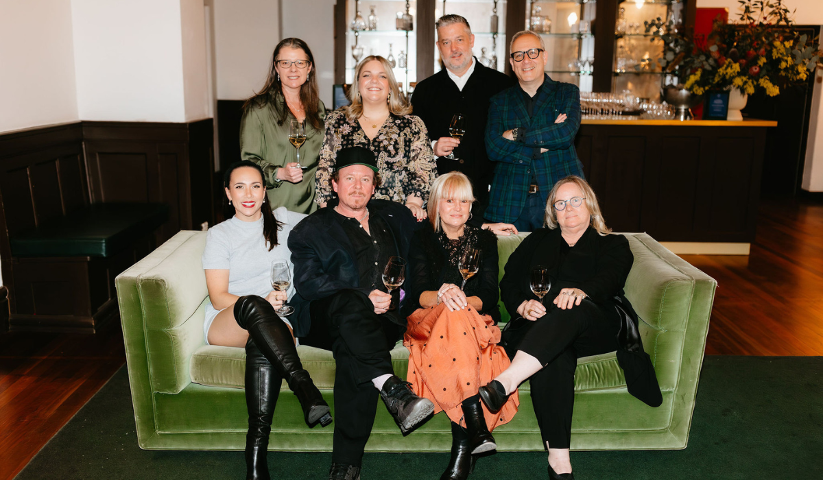 The Halliday Tasting Team sit on or stand behind a green velvet couch