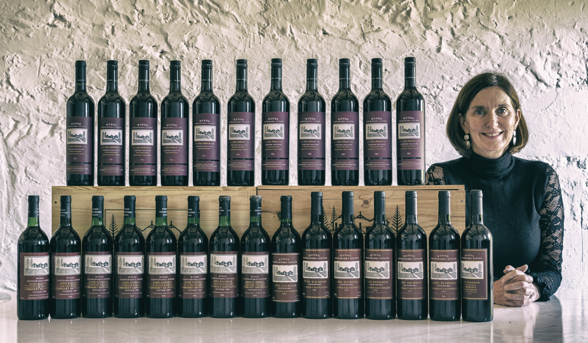 A woman stands with back vintages of a wine