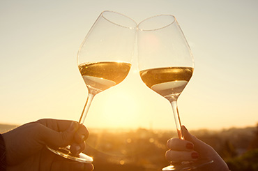 Two people making a toast with white wine at sunset.