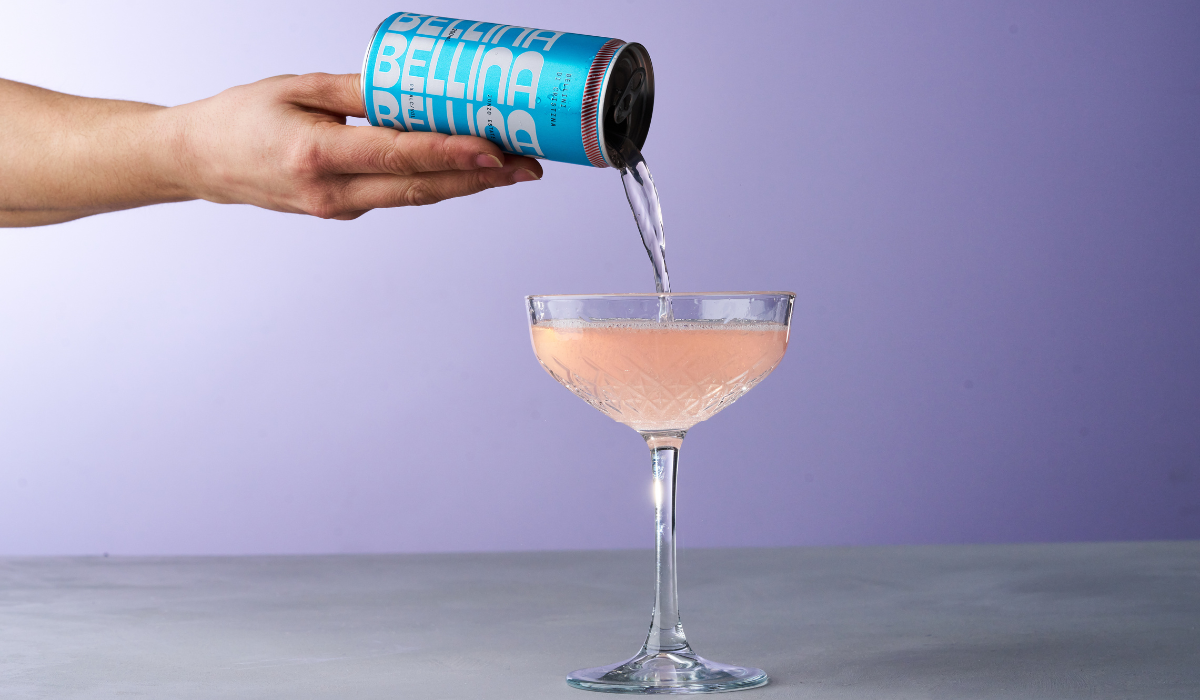 A pink canned cocktail being poured into a coupe glass