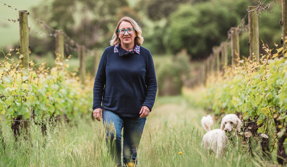 A woman and her dog walk among grapevines