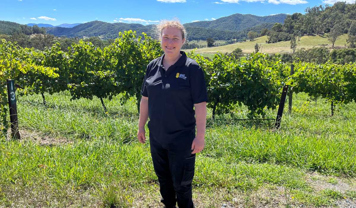 A woman stands in front of some grape vines