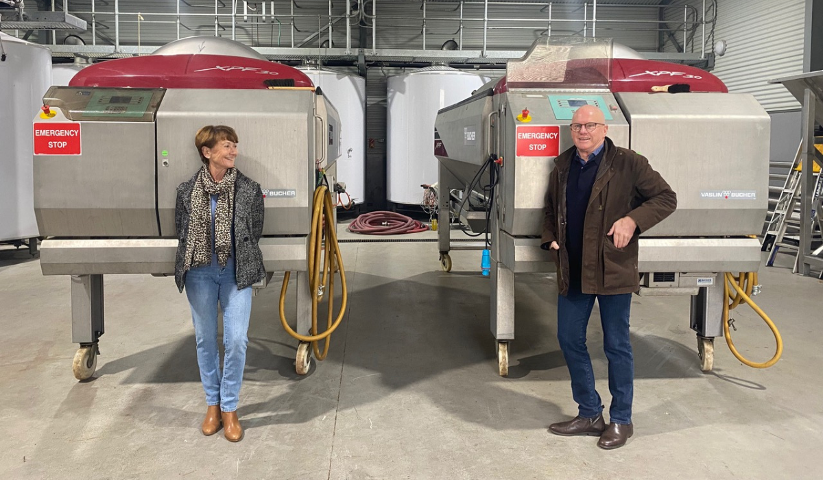 A woman and a man stand in front of two wine presses