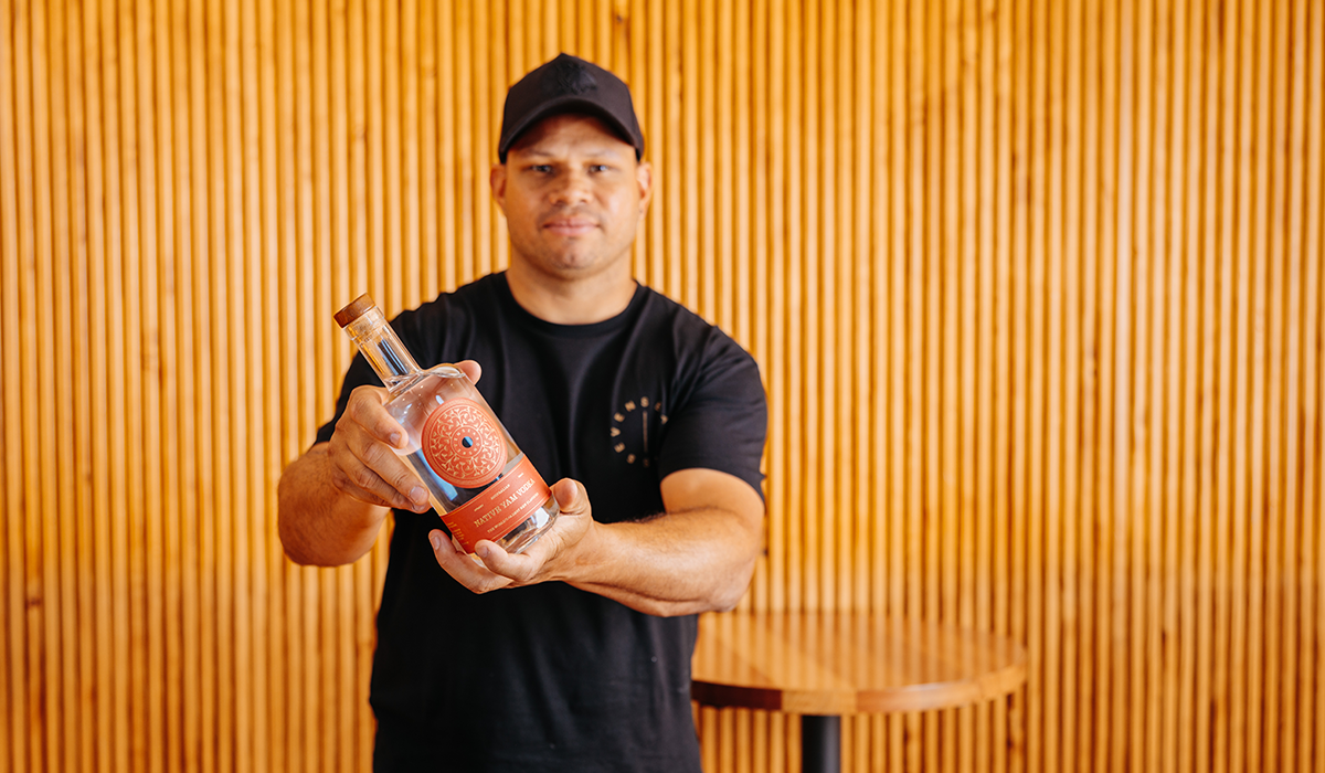 Daniel Motlop wearing a black tshirt and black cap, holding a bottle of Seven Season gin.