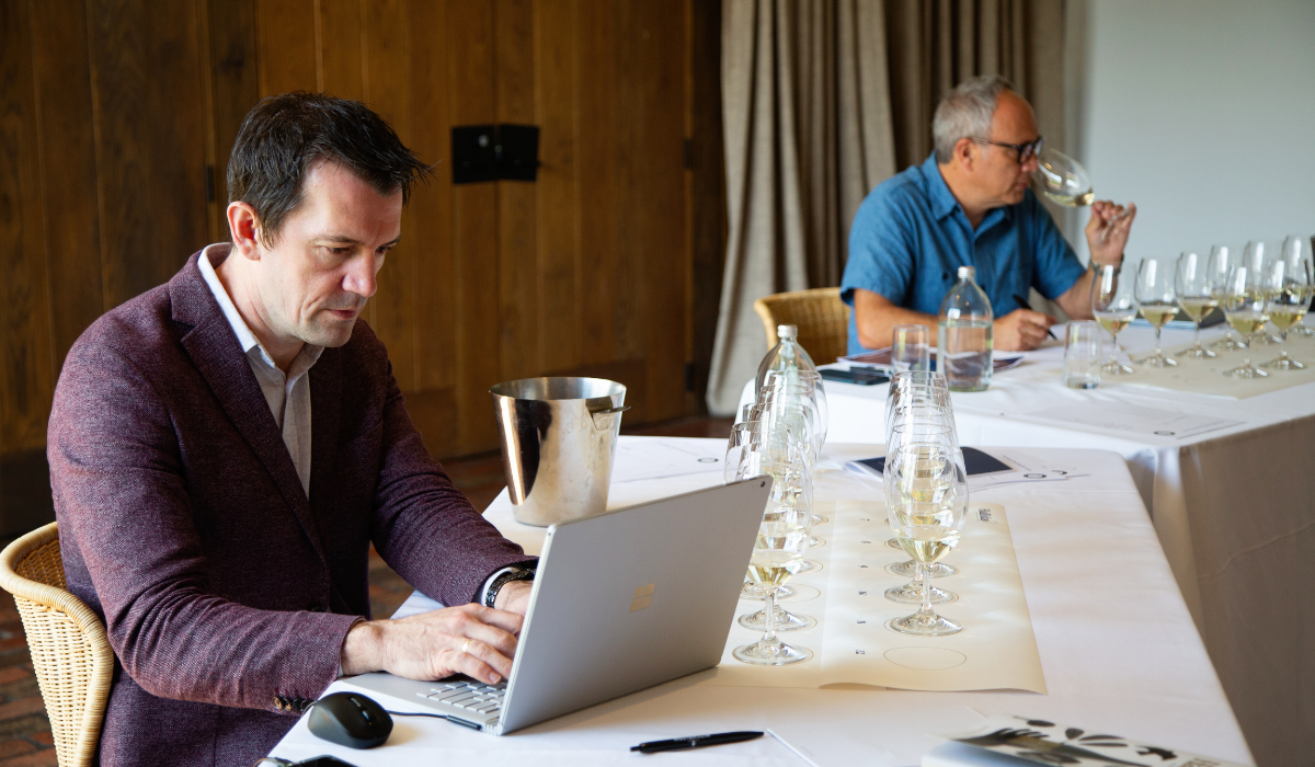 Two men sit at a table tasting white wine