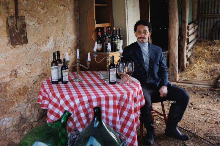 Fabiano Minchella sits at a table covered in a red and white checkered tablecloth with his range of wines on top