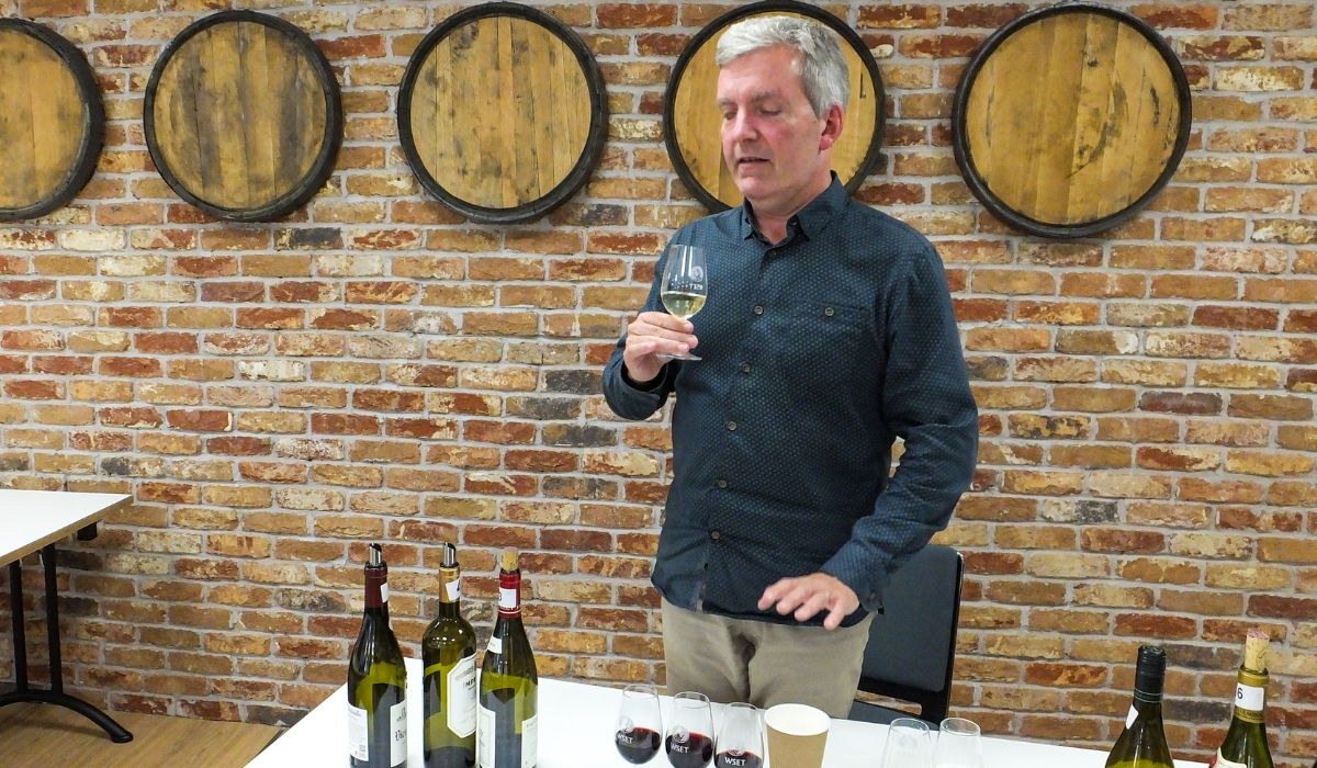 A man stands behind a table; the table is covered with wine glasses and bottles