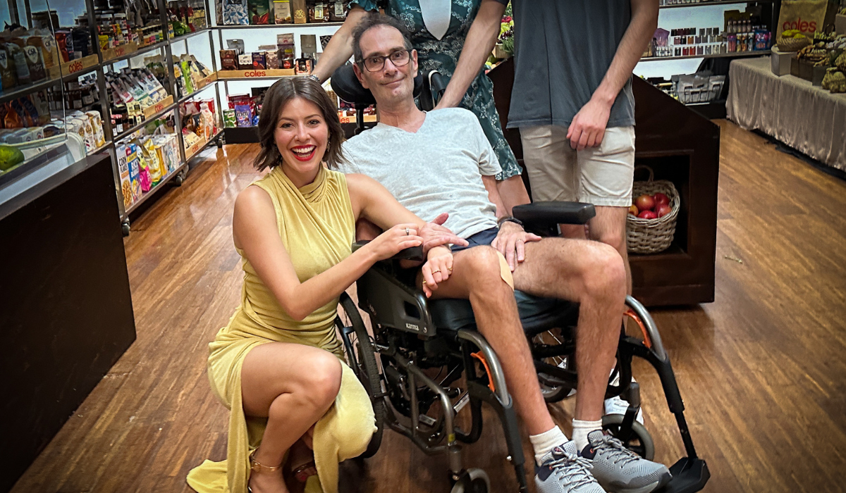 A girl crouches down next to a man in a wheelchair 