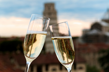 Two glasses of sparkling toasting with an Italian scene in the background