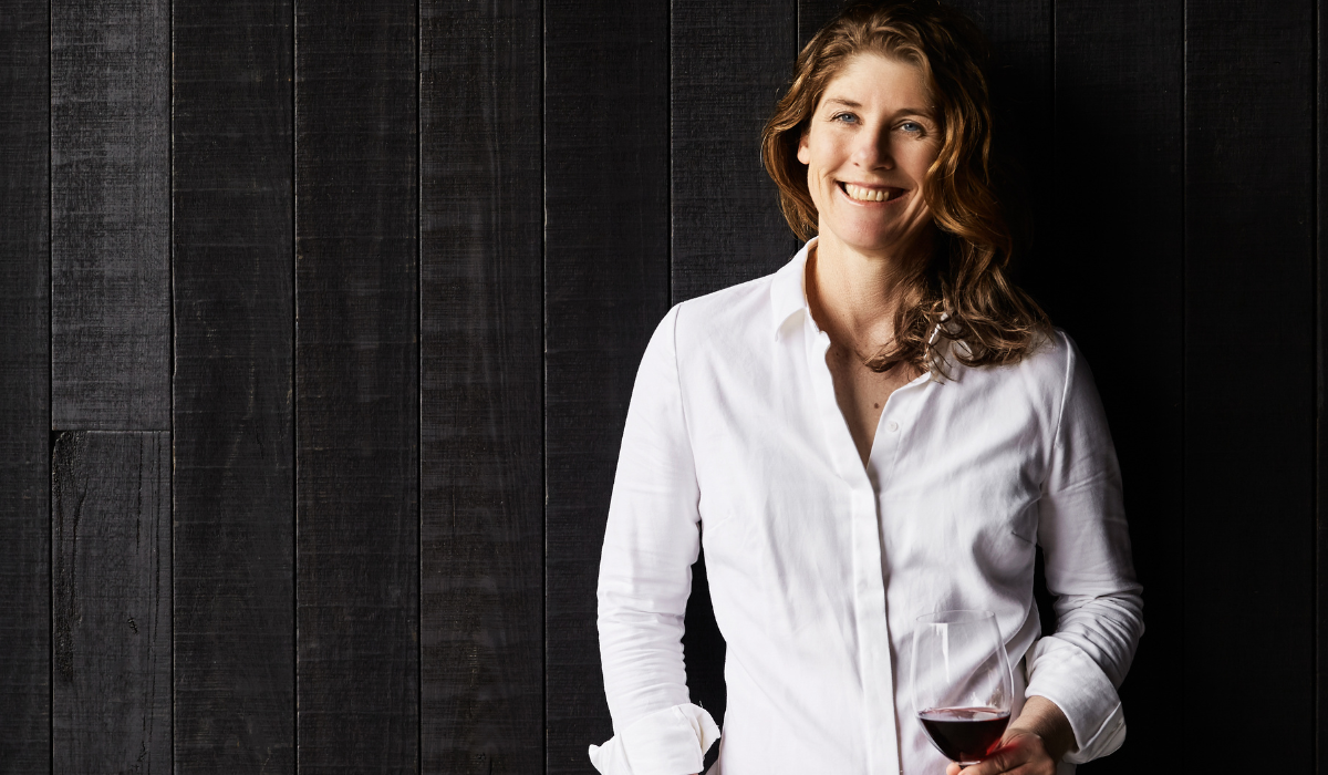 A woman wears a white shirt and holds a glass of red wine 