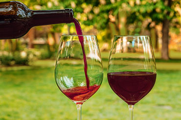 Light red wine being poured into glasses with a park in the background