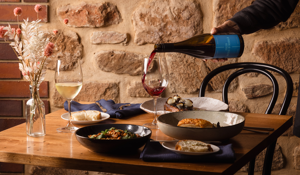 A bottle of O'Leary Walker being poured into a glass, surrounded by food and glasses of wine