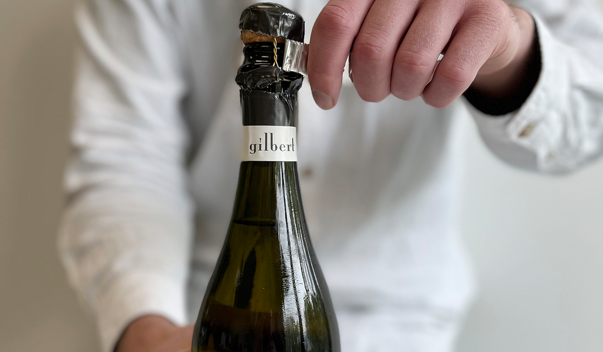 A bottle of Gilbert sparkling wine with the foil being removed from the neck of the bottle