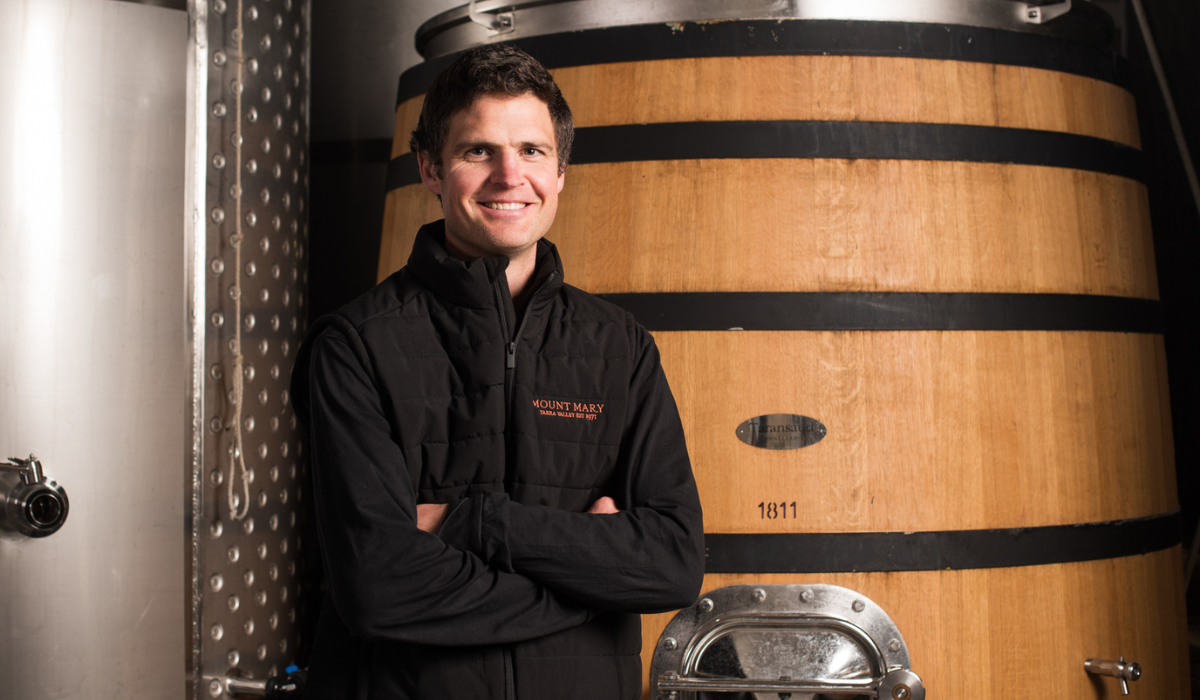 A man crosses his arms in front of a wine barrel