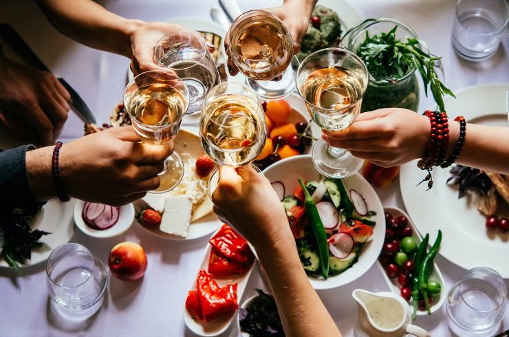Bird's eye view of white wine glasses being clinked over a table laid with food