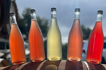 Five bottles of pet nat on a barrel