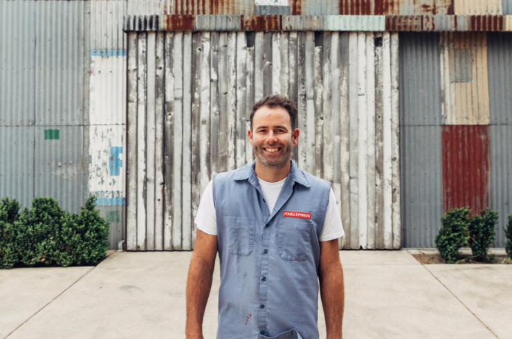 A male winemaker smiles in front of his winemaking shed