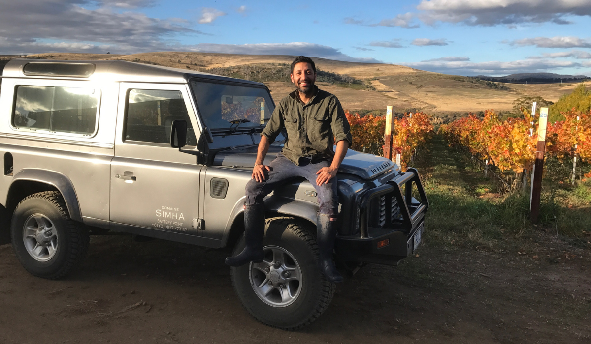 A man sits on the bonnet of his four-wheel drive in front of vineyards