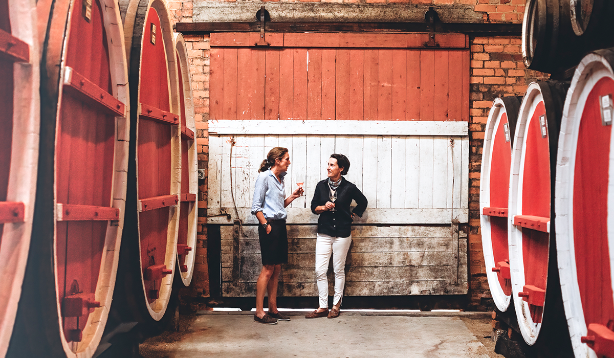 Two women talking, surrounded by wine barrels