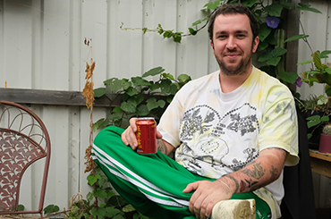Jack Shaw sitting down with his knee crossed over his other leg, holding a can of beer