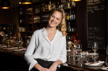 A woman wearing a white shirt stands in front of a bar