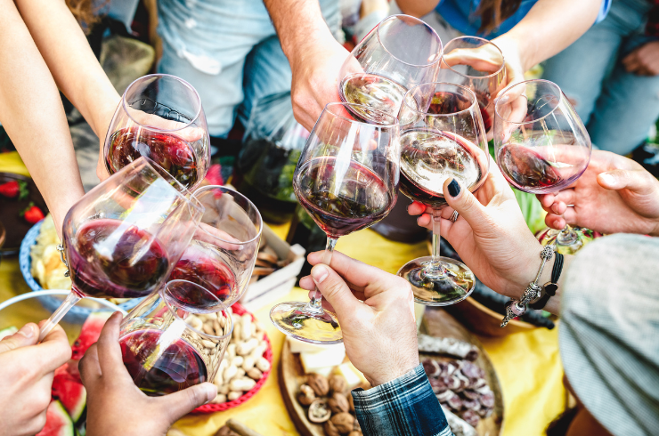 Many hands hold glasses of red wine, cheersing