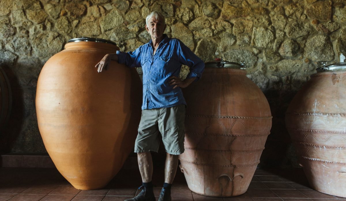 A winemaker stands in front of two large ceramic amphorae