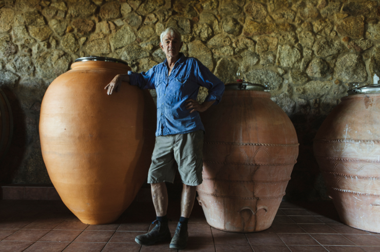 A winemaker stands in front of two large ceramic amphorae