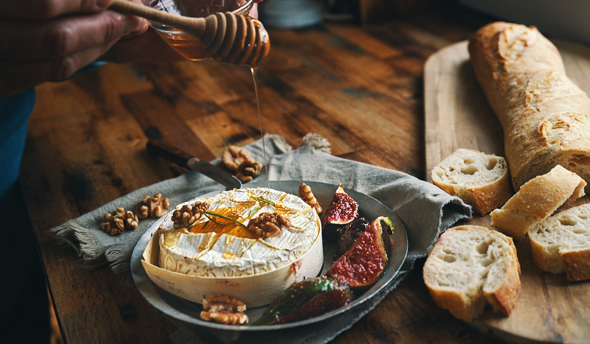 Camembert being drizzled with honey and bread to the side.