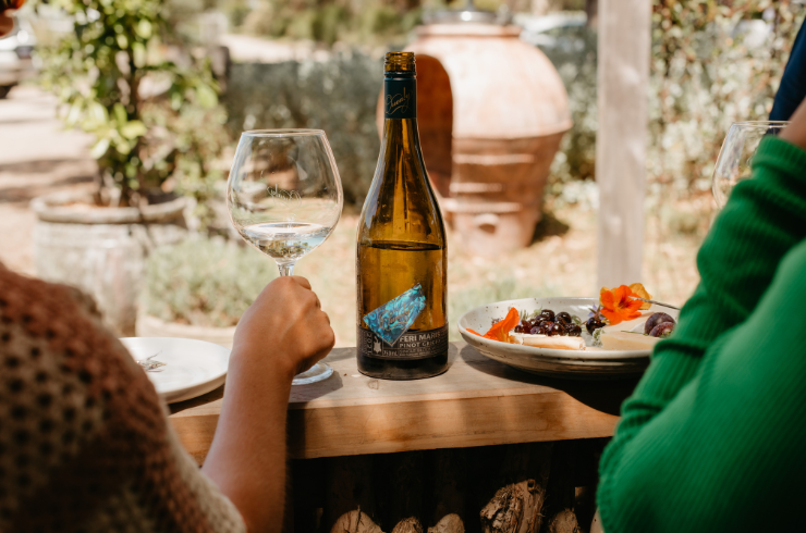 A bottle of white wine and a cheese platter rest on a deck