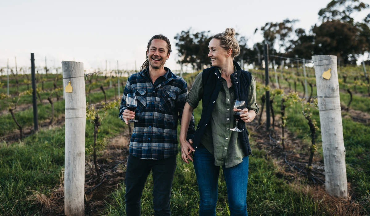 A male and female winemaker stand in a vineyard