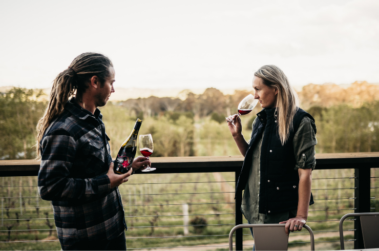 A man and a woman drink red wine overlooking a vineyard