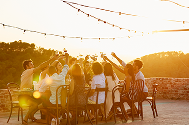 A group a friends around a table toasting wine in the sun