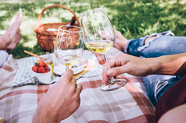 Two people on a picnic rug with glasses of white wine