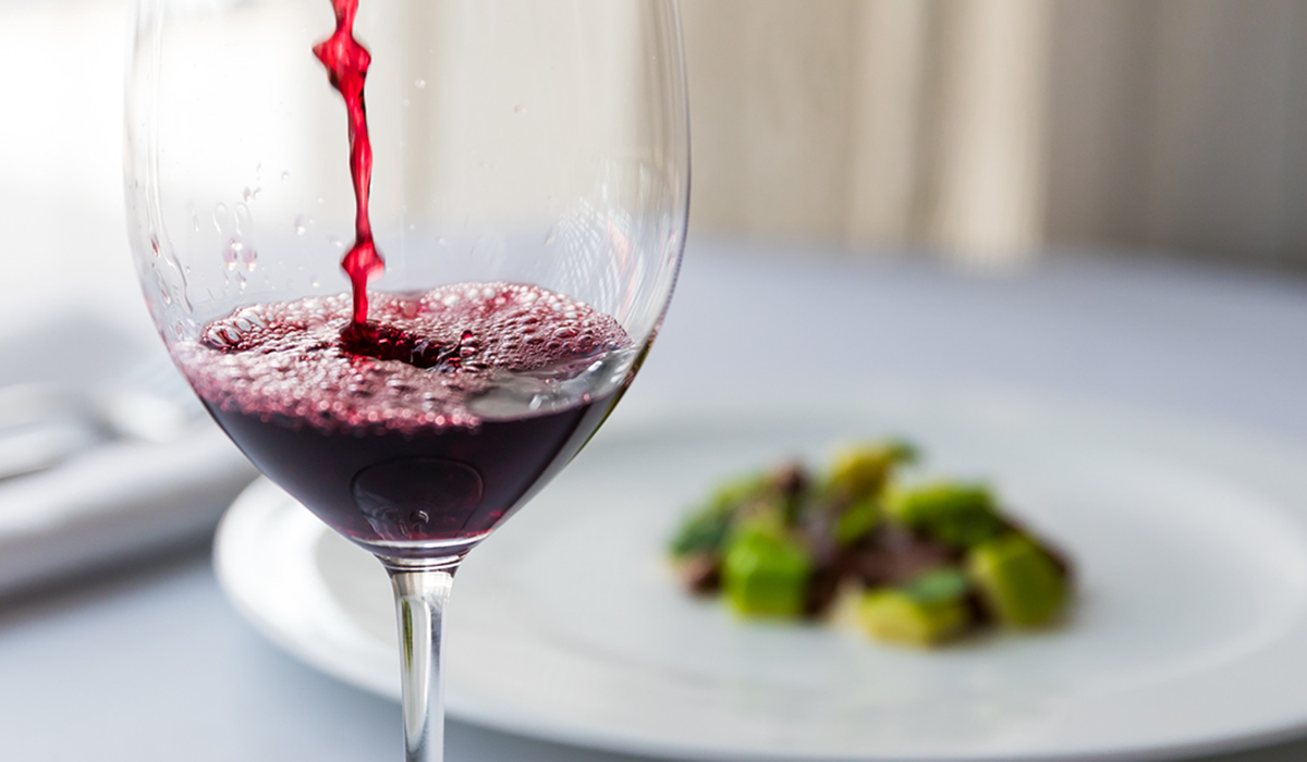 A glass of shiraz with a plate of food in the background