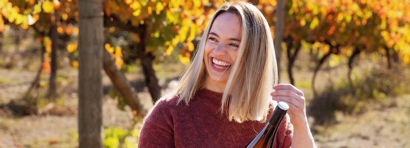 A smiling woman holidng at bottle of PachaMama in the vineyard